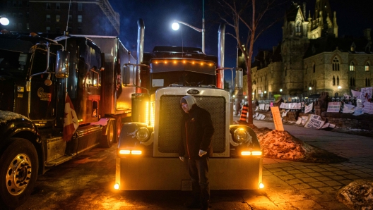 TOPSHOT - A truck driver listens to the engine of his truck during a protest over pandemic health rules and the Trudeau government, outside the parliament of Canada in Ottawa on February 14, 2022. - Canadian Prime Minister Justin Trudeau on Monday invoked rarely used emergency powers to bring an end to trucker-led protests against Covid health rules, after police arrested 11 people with a "cache of firearms" blocking a border crossing with the United States. (Photo by Ed JONES / AFP)