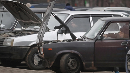 epa09607241 A toy Kalashnikov assault rifle stick supports a carâ??s open hood as a young man repairs his rusty old Lada, a  brand of cars manufactured by AvtoVAZ, in Moscow, Russia, 27 November 2021. Old Lada vehicles often become the first car owned by thousands of young people in Russia.  EPA/MAXIM SHIPENKOV