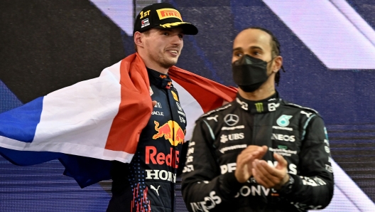 TOPSHOT - 2021 FIA Formula One World Champion Red Bull's Dutch driver Max Verstappen walks past second-placed Mercedes' British driver Lewis Hamilton (R) on the podium of the Yas Marina Circuit after the Abu Dhabi Formula One Grand Prix on December 12, 2021. - Max Verstappen became the first Dutchman ever to win the Formula One world championship title when he won a dramatic season-ending Abu Dhabi Grand Prix at the Yas Marina circuit on December 12, 2021. The Red Bull driver won his 10th race of the season to finish ahead of seven-time champion Lewis Hamilton. (Photo by ANDREJ ISAKOVIC / AFP)