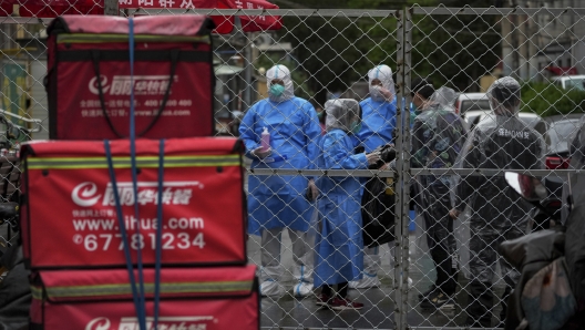 Health workers wearing protective gear chat with security guards behind a barricaded fence of a locked down communities on Wednesday, April 27, 2022, in Beijing. Workers put up fencing and police restricted who could leave a locked-down area in Beijing on Tuesday as authorities in the Chinese capital stepped up efforts to prevent a major COVID-19 outbreak like the one that has all but shut down the city of Shanghai. (AP Photo/Andy Wong)