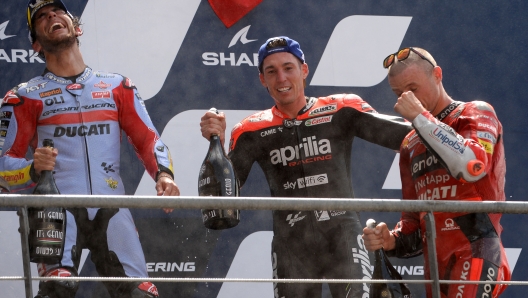 Second placed Ducati Lenovo Australian rider Jack Miller (R), first placed Gresini Racing Italian rider Enea Bastianini (L), and third placed Aprilia Spanish rider Aleix Espargaro (R) celebrate with champagne on the podium after the French Moto GP Grand Prix, at the Bugatti circuit in Le Mans, northwestern France, on May 15, 2022. (Photo by JEAN-FRANCOIS MONIER / AFP)