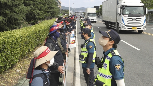 Members of Cargo Truckers Solidarity hold signs as police officers stand guard outside of Hyundai Motor plant in Ulsan, South Korea, Wednesday, June 8, 2022. (Kim Yong-tai/Yonhap via AP)