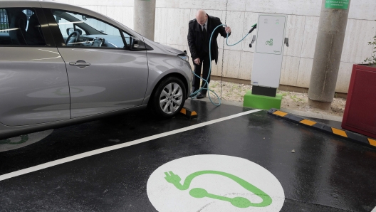 (FILES) In this file photo taken on March 17, 2014 a man plugs his car in Paris, at the charging station for electric vehicles dedicated to public services staff at the French economic and financial ministries after its inauguration. - With summer holidays looming, Europe's electric car owners may be wondering whether to risk taking their vehicles for long journeys. AFP investigates the pitfalls and joys of long-distance emissions-free motoring. (Photo by Jacques DEMARTHON / AFP)