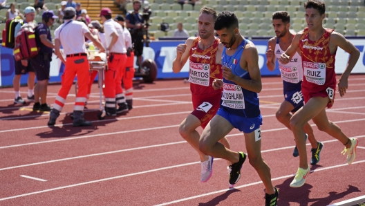 Osama Zoghlami, of Italy, center, competes while Axel Vang Christensen, of Denmark, background left, is taken away on a stretcher after getting injured in a Men's 3000 meters steeplechase heat during the athletics competition in the Olympic Stadium at the European Championships in Munich, Germany, Tuesday, Aug. 16, 2022. (AP Photo/Matthias Schrader)