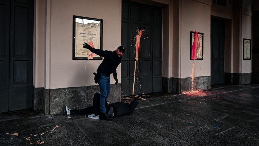 A police officer detains an environmental activist from the "Last Generation" (Ultima Generazione) group after several activists smeared with paint the facade of the La Scala theatre during a group's action in Milan on December 7, 2022, aimed at raising awareness about climate change on the day of La Scala's new season's opening. (Photo by Piero CRUCIATTI / AFP)