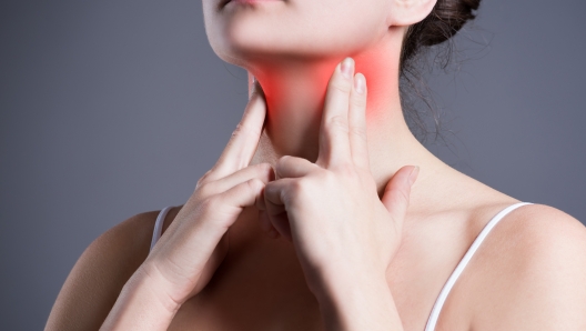 Sore throat, woman with pain in neck, gray background, studio shot