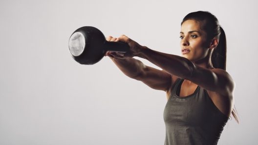 Young fitness female exercise with kettle bell. Mixed race woman doing gym workout on grey background