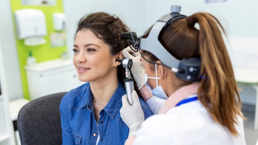 Hearing exam. Otolaryngologist doctor checking woman's ear using otoscope or auriscope at medical clinic. Otorhinolaryngologist pulling ear with hand and looking at it with otoscope closeup.