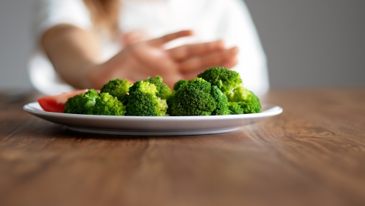 No vegan diet concept. Teen girl pushing away plate with broccoli and other vegetables refusing to eat. Food waste. Copy space. Selective focus on food.