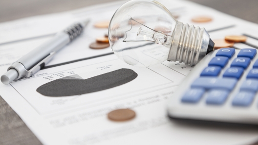 A light bulb, a pen, a calculator and some copper euro cent coins lie on top of an electricity bill.