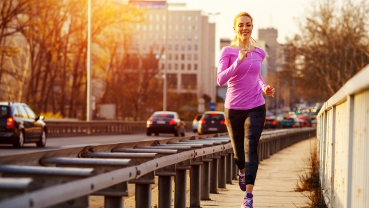 Young beautiful woman running on the sidewalk besides traffic road in the city