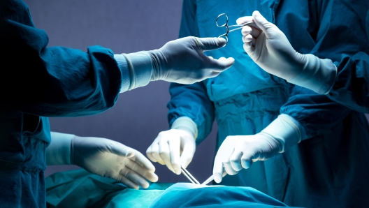 doctor and nurse medical team are performing surgical operation at emergency room in hospital. assistant hands out scissor and instruments to surgeons during operation.