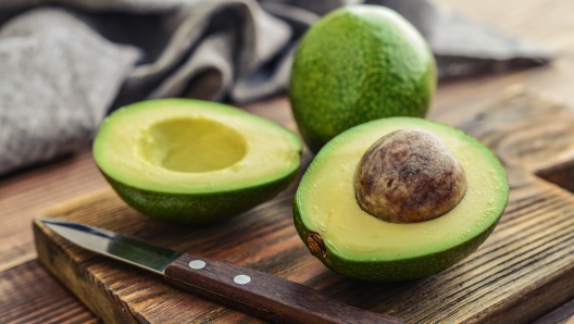 Fresh avocado on cutting board over wooden background