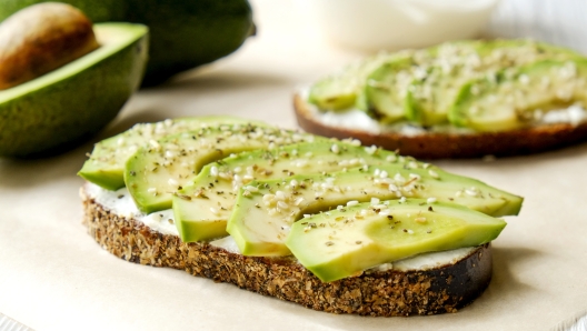 Vegan sandwich, rye bread toast, avocado slices, vegenaise sauce & raw arugula. Toasted sourdough, eggless mayonnaise, wooden table, whole & halved. National avocado day concept. Close up, background.