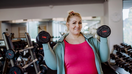 A plus size woman training and lifting dumbbells indoors in gym, looking at camera