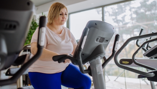 A happy mid adult overweight woman exercising on stepper indoors in gym