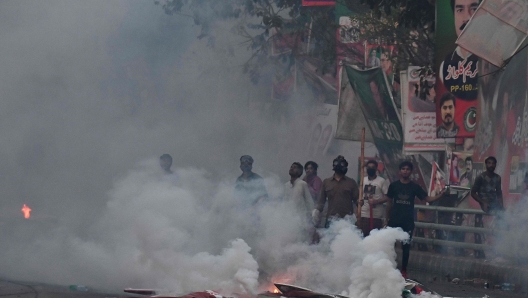 Supporters of former prime minister Imran Khan gather amid teargas fired by riot police outside Khan's house to prevent officers from arresting him, in Lahore on March 14, 2023. (Photo by Arif ALI / AFP)