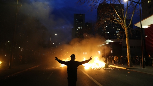 A protester walks past burning garbages during a protest in Paris, Saturday, March 18, 2023. A spattering of protests were planned to continue in France over the weekend against President Macron's controversial pension reform, as garbage continued to reek in the streets of Paris and beyond owing to continuing action by refuse collectors. (AP Photo/Lewis Joly)