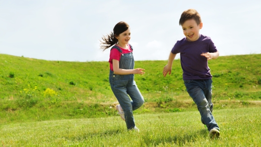 summer, childhood, leisure and people concept - happy little boy and girl playing tag game and running outdoors on green field