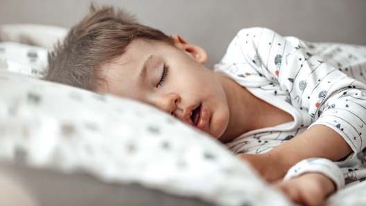 Little blond boy sleeping in his bed. Restless sleep of a baby with a cold. The kid sleeps with his mouth open. My little boy sleeping by the light of the window.