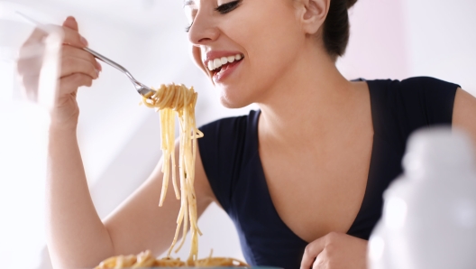 Young woman eating tasty pasta in restaurant