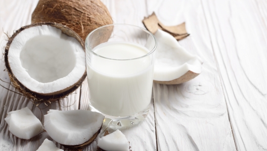 Drinking glass of milk or yogurt on blue napkin on white wooden table with coconut aside