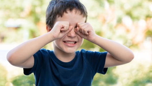 Child suffering itching scratching eyes outdoors in a park