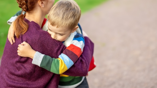 Child with rucksack and with mother in front of a school building. Concept of motherhood and beginning of primary school.