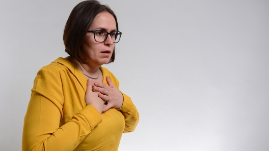 Pretty brunette woman having breath difficulties in front of white background. A young woman holding her breast in pain