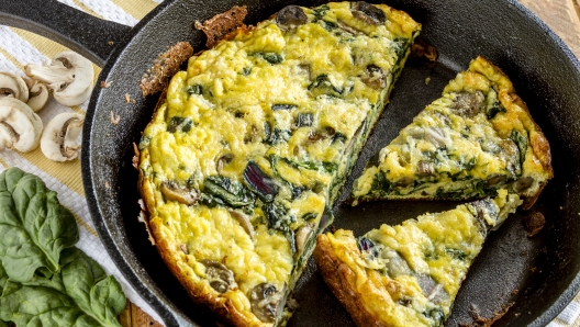 Close up of spinach mushroom frittata sitting on yellow striped kitchen towel with raw ingredients