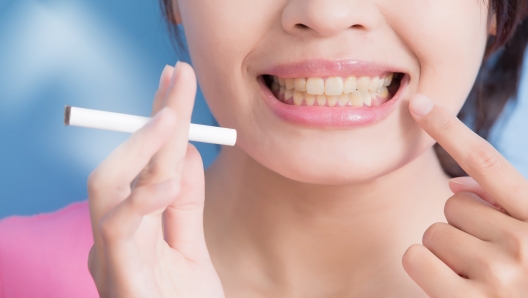 Woman holding cigarettes with yellow teeth isolated on blue background, asian