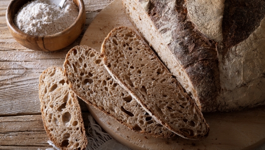 Traditional bread, Sliced wholemeal loaf on cutting board, with bowl of flour on old wooden table, closeup.