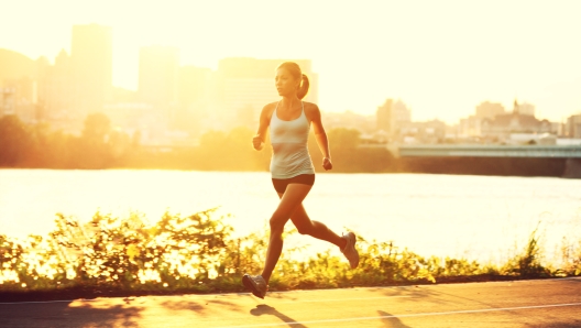 female runner running at sunset in city park. Healthy fitness woman jogging outdoors. Montreal skyline in background.