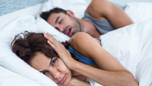 Portrait of woman blocking ears with hands while man snoring on bed