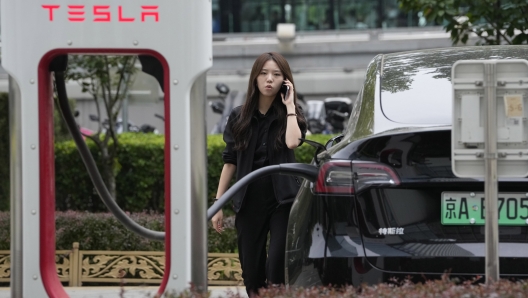 A worker stands next to a Tesla being charged in Beijing, Tuesday, May 30, 2023. China?s foreign minister met Tesla Ltd. CEO Elon Musk on Tuesday and said strained U.S.-Chinese relations require ?mutual respect,? while delivering a message of reassurance that foreign companies are welcome. (AP Photo/Ng Han Guan)