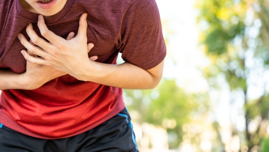 Exhausted male runner athlete suffering painful angina pectoris or asthma breathing problems while running in the park.