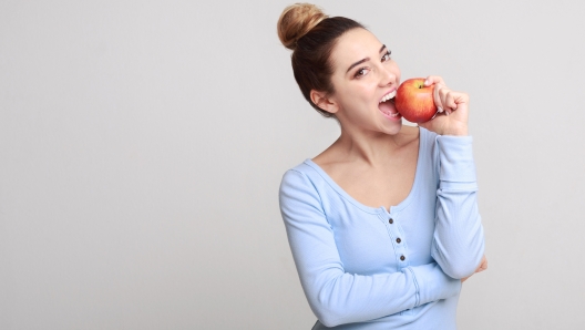 Healthy eating. Pretty girl biting fresh apple over grey background, copy space