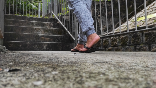 Female feet in long pants and black flip flops stepped on the concrete floor towards the stairs with an iron fence.