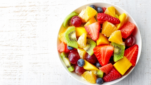 Bowl of healthy fresh fruit salad on wooden background. Top view.