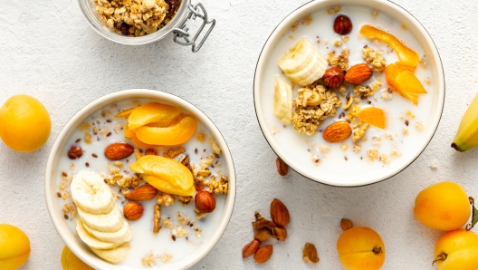 Healthy breakfast cereal top view. Granola breakfast with fruits, nuts, milk and peanut butter in bowl on a white background