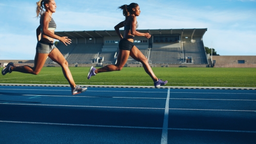 Athletes arrives at finish line on racetrack during training session. Young females competing in a track event. Running race practicing in athletics stadium.