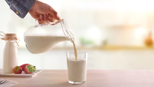 Serving breakfast milk with a jug in a glass on a white wooden kitchen table. Horizontal composition. Front view