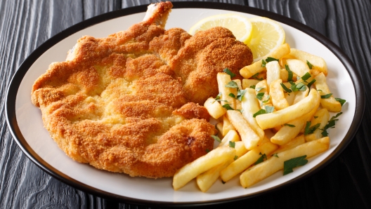 Fried veal cutlet Milanese with lemon and French fries close-up on a plate on a table. Horizontal