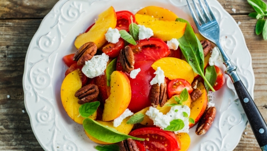 Summer peach tomato salad with basil, baby spinach, feta cheese and pecan nuts. Summer appetizer food. Picnic outdoor concept