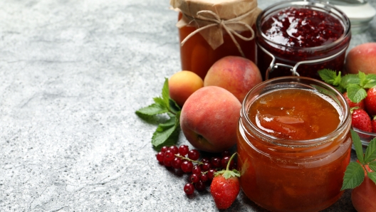 Jars with different jams and fresh fruits on grey table. Space for text