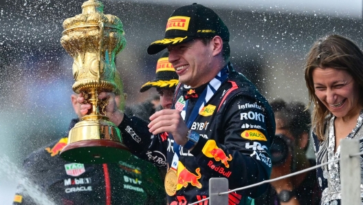 Winner Red Bull Racing's Dutch driver Max Verstappen holding the trophy reacts as second placed McLaren's British driver Lando Norris sprays champagne during the podium ceremony for the Formula One British Grand Prix at the Silverstone motor racing circuit in Silverstone, central England on July 9, 2023. (Photo by Ben Stansall / AFP)