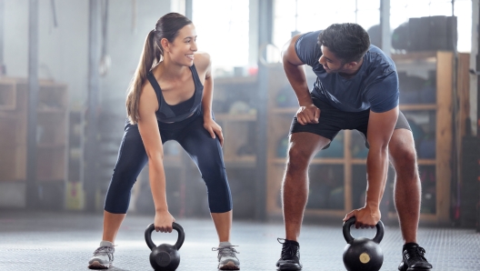 Strong, wellness couple doing kettlebell weight exercise, workout or training inside a gym. Happy sports people or trainer motivation, exercising with fitness equipment for muscle, strength or health