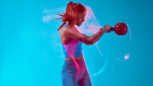 A female bodybuilder lifting kettlebell in studio. Long exposure movement capture.