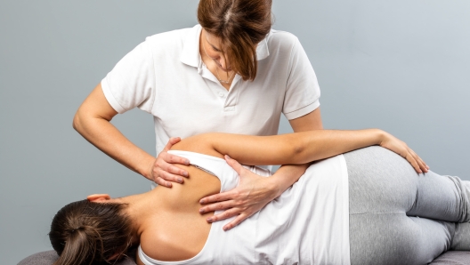 Close up of female osteopath doing shoulder blade therapy on young woman.