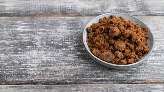 plate with unrefined brown cane sugar on gray wooden background. side view, copy space.